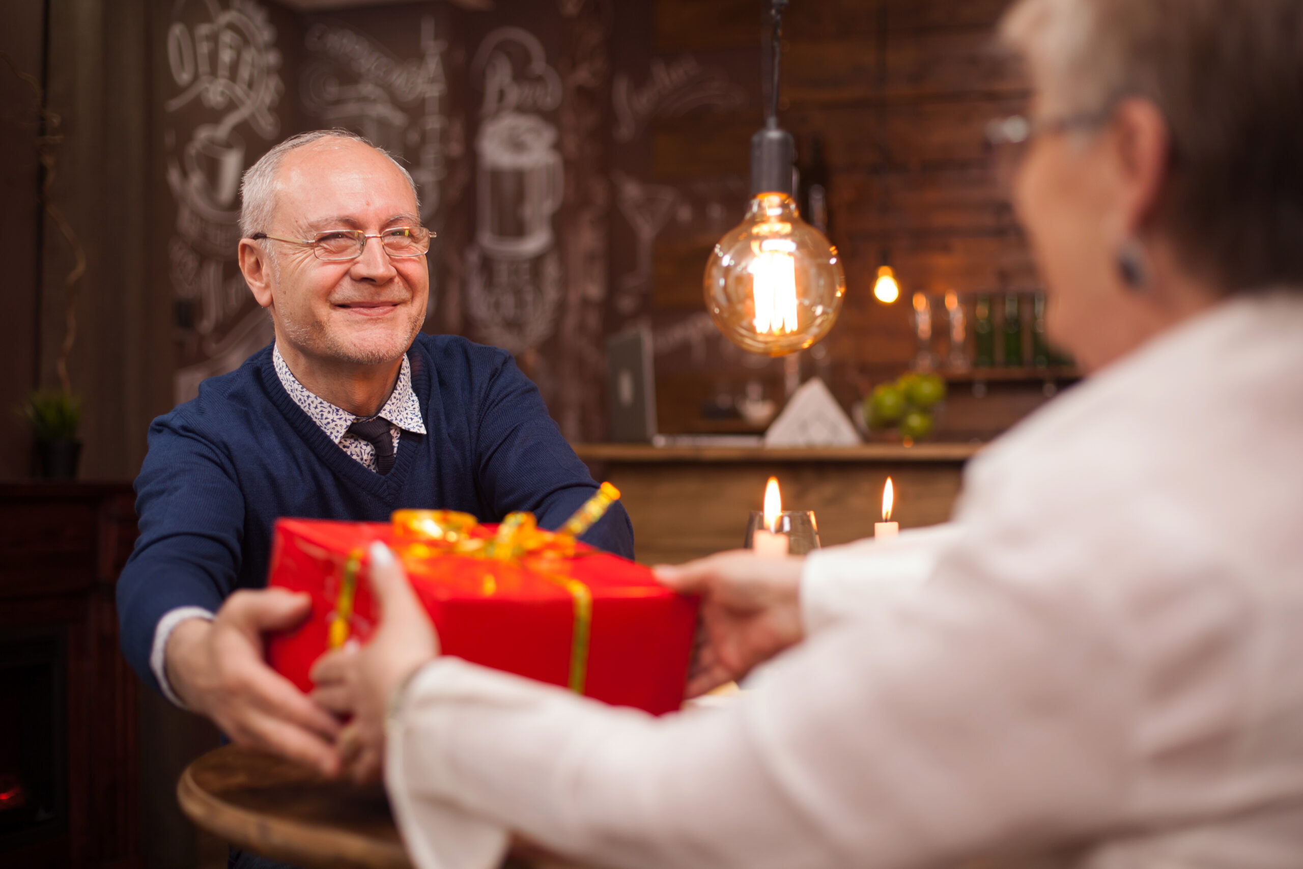 Retired old couple having a good time during dinner. Husband giving her wife a gift.